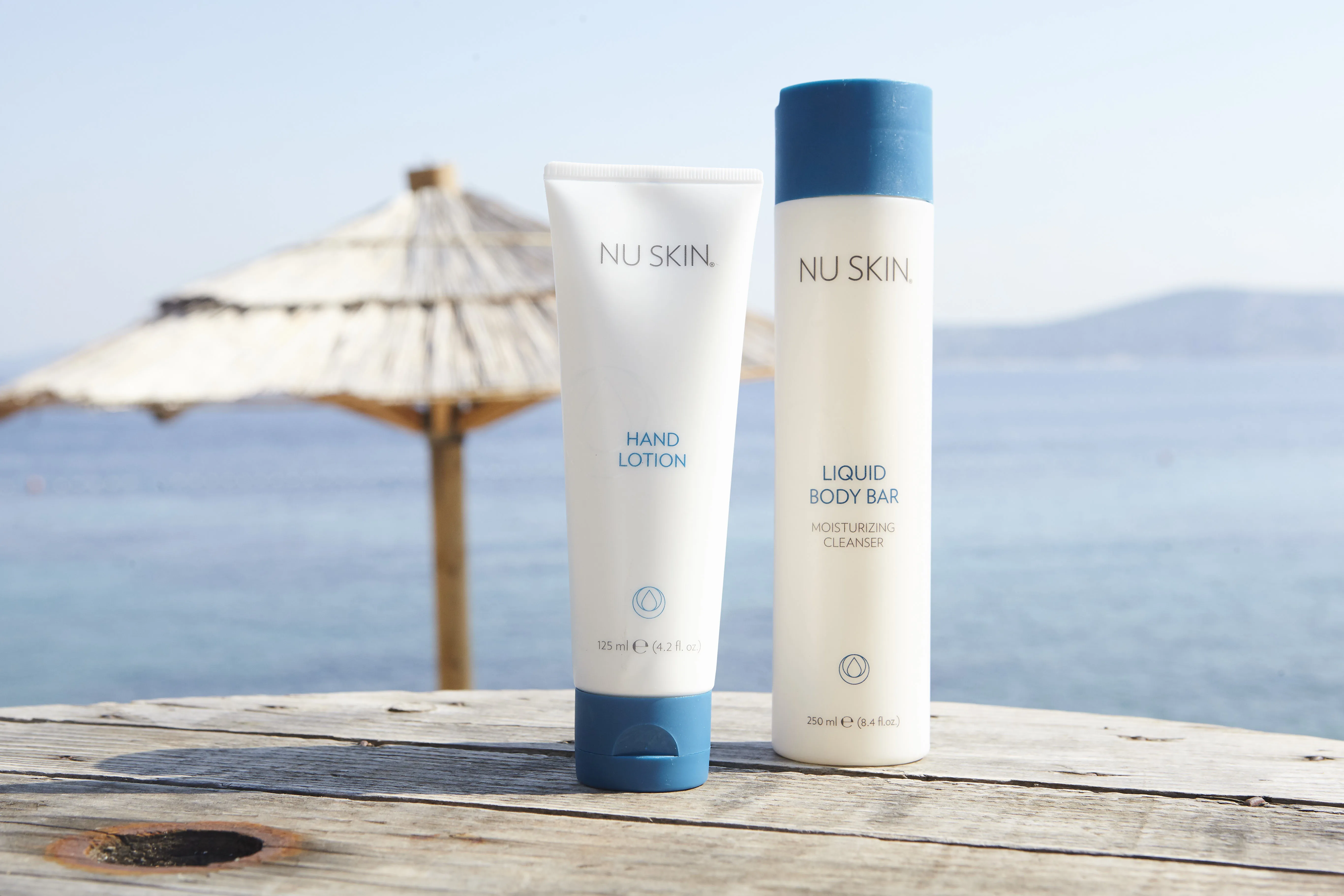 Nu Skin Produkte auf Steg vor Meer und Sonnenschirm