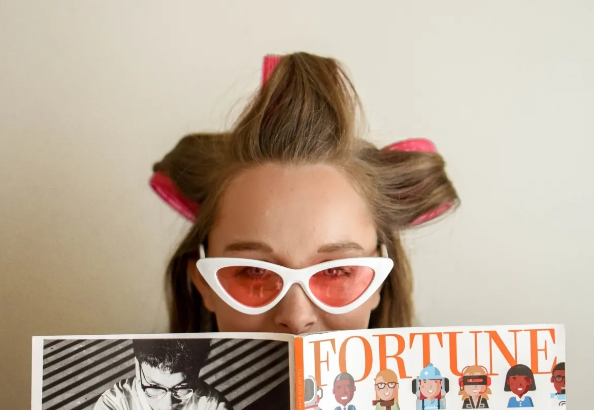 Frau mit Sonnebrille und Lockenwicklern liest ein Magazin